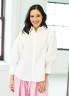 Woman wearing a white blouse and pink pants in an indoor setting