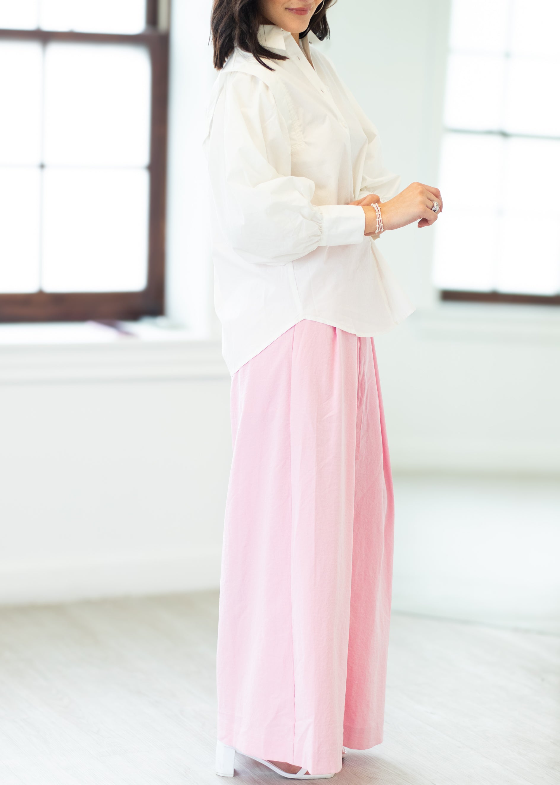 Person wearing a white blouse and pink skirt in a bright room.