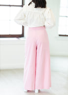 Person wearing a white blouse and pink pants in a minimal indoor setting