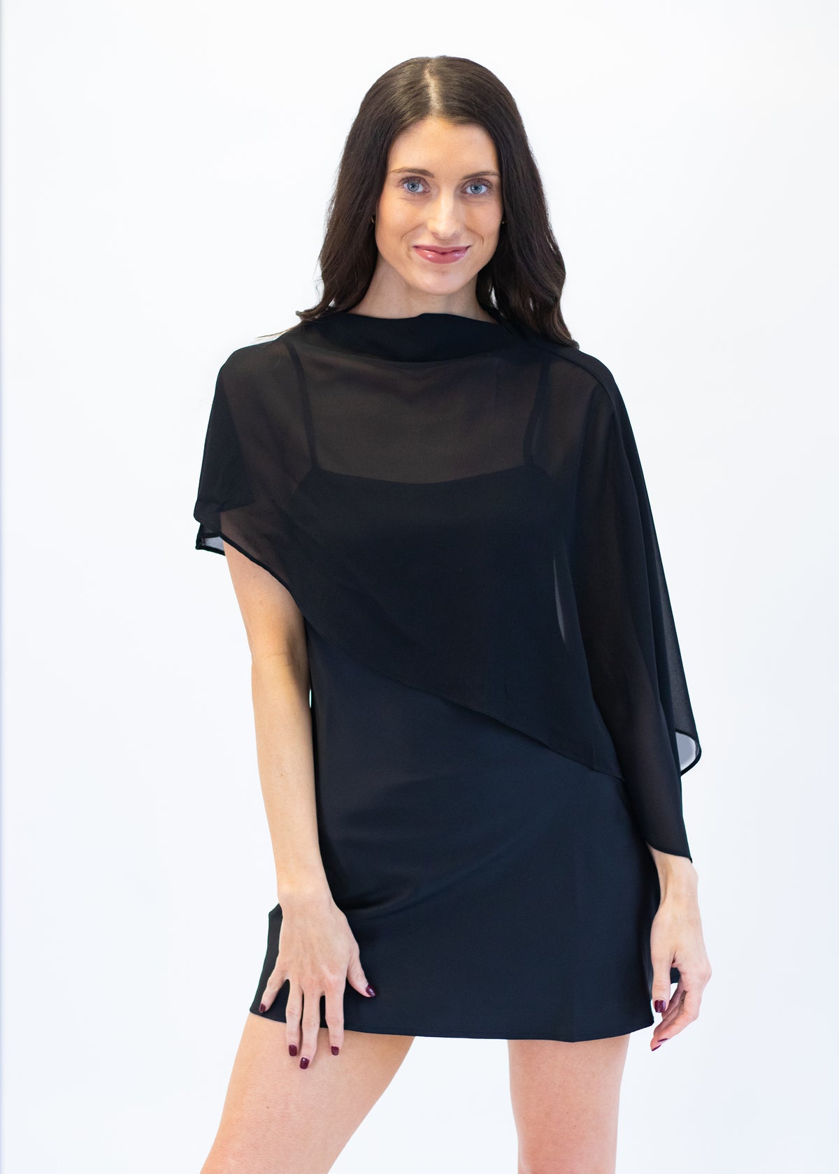 A woman modeling a black sheer overlay dress with short flutter sleeves and a draped, asymmetrical wrap-style skirt, photographed against a plain white studio background.