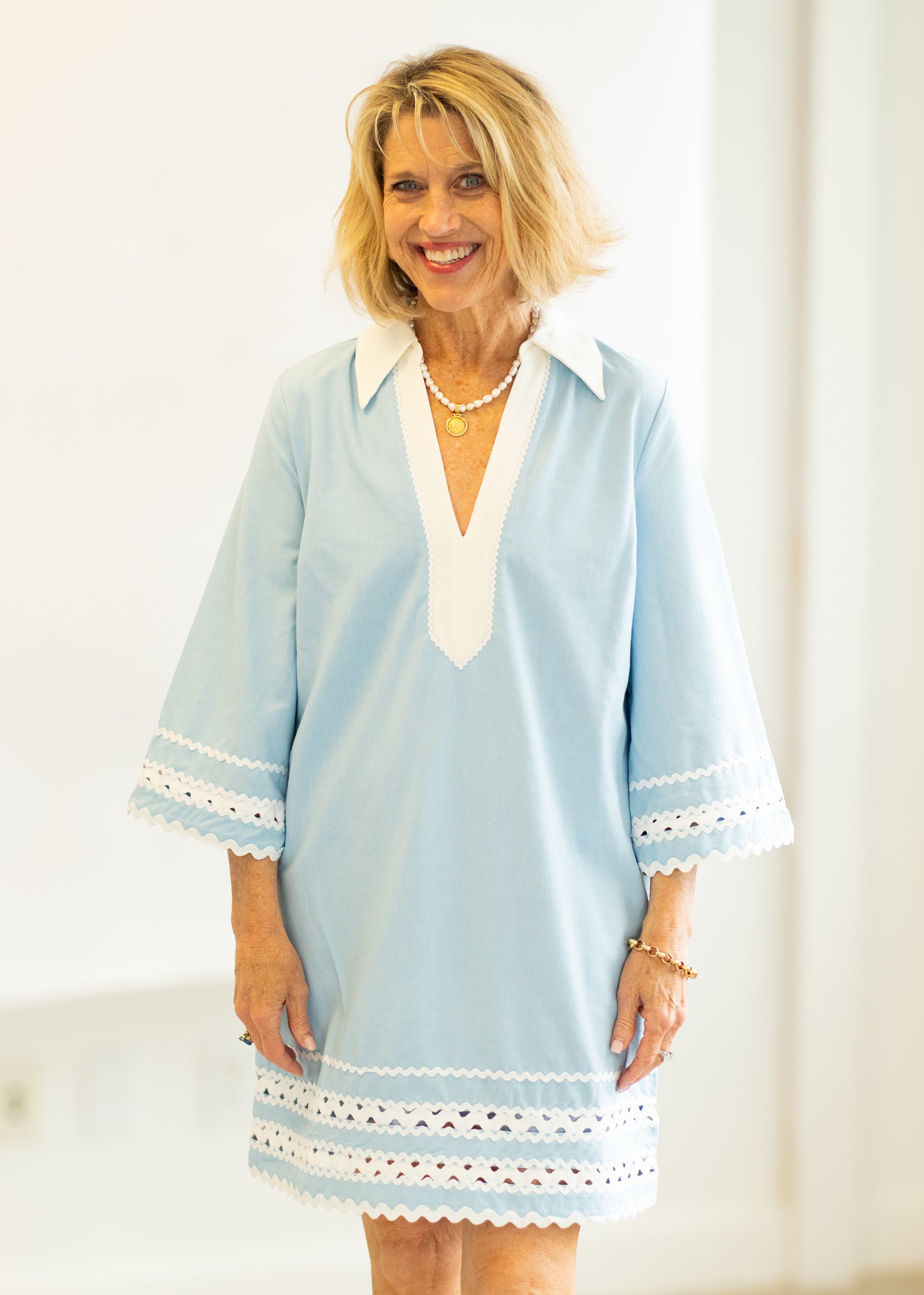 Woman wearing a light blue dress with white accents against a plain background