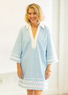 Woman wearing a light blue dress with white accents against a plain background