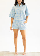 Person wearing a light blue patterned shirt and shorts set on a white background