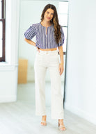 Woman wearing a striped blouse and white pants in a bright room.