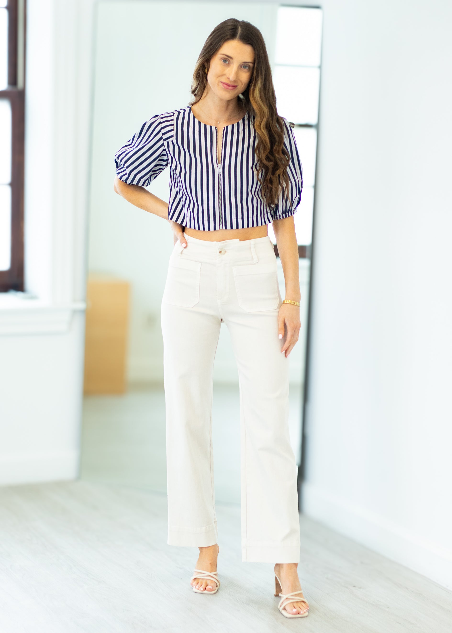Woman wearing a striped blouse and white pants in a bright room.