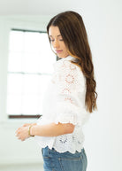 Woman wearing a white lace top and blue jeans indoors