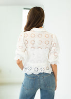 Person wearing a white lace top and blue jeans against a plain background