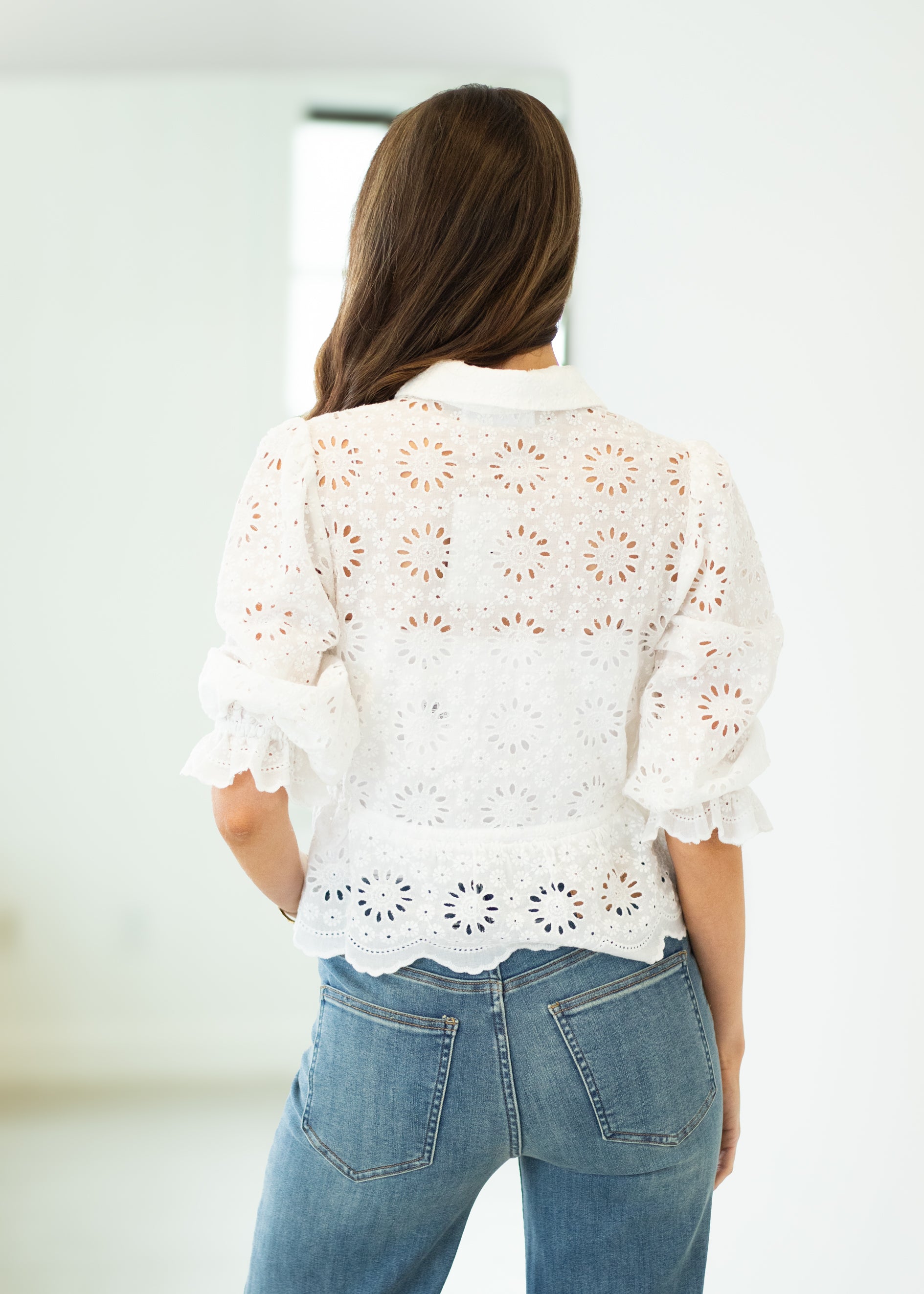 Person wearing a white lace top and blue jeans against a plain background