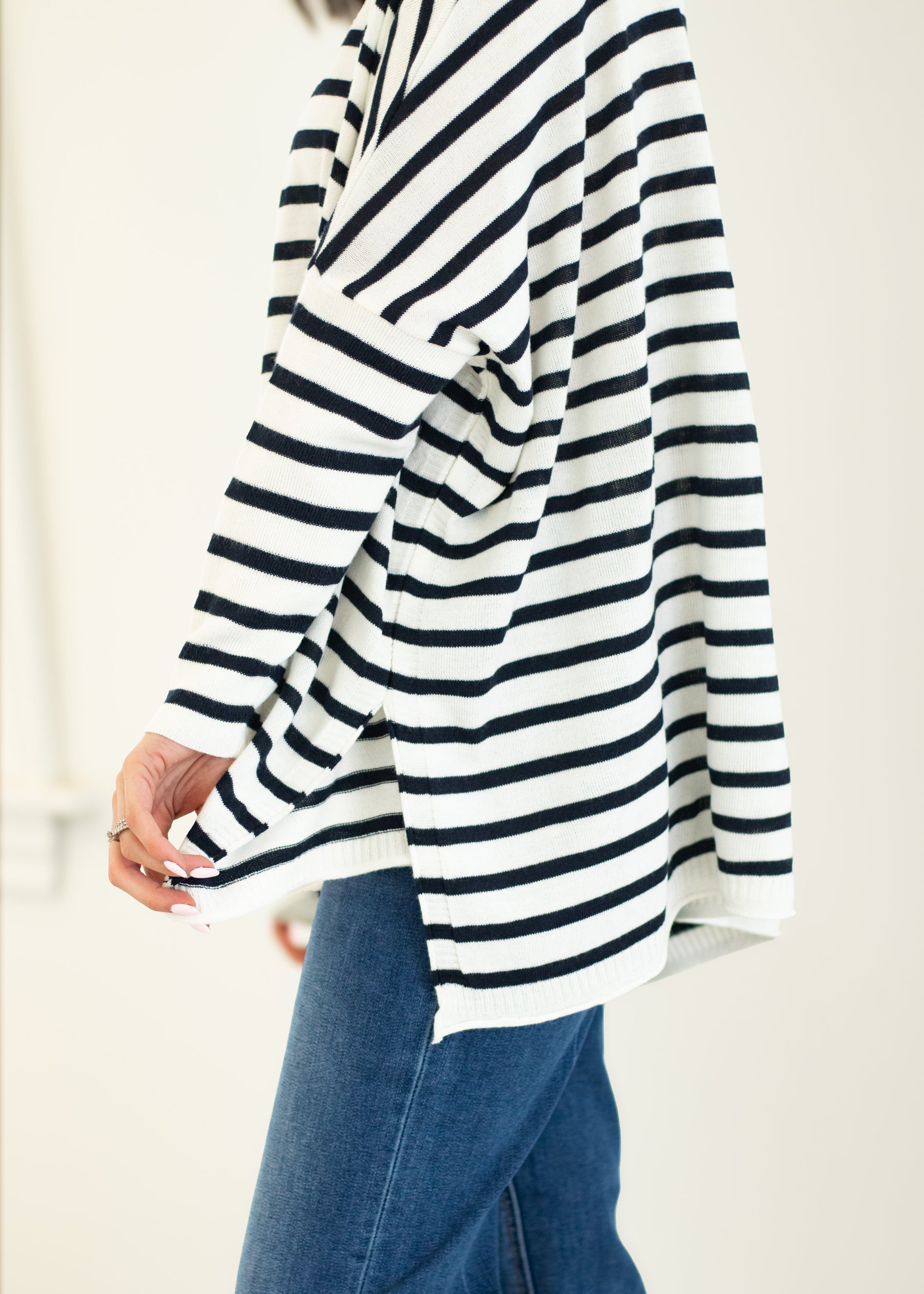 Person wearing a black and white striped long-sleeve top with blue jeans on a plain background