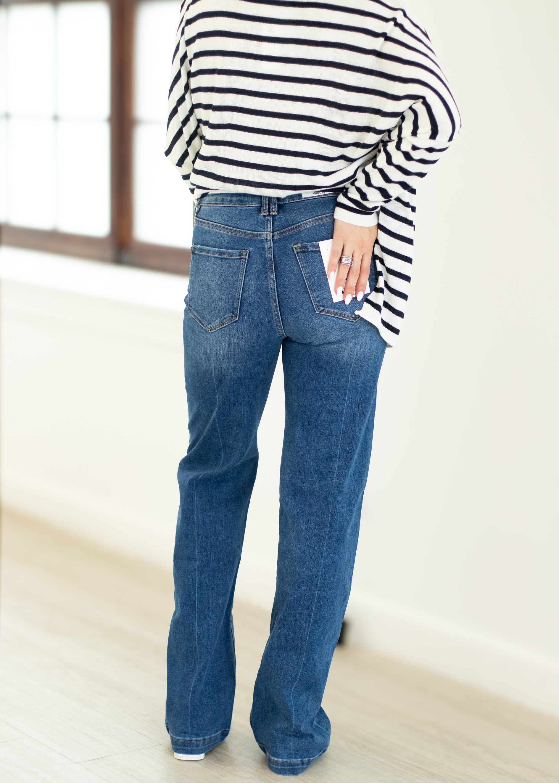 Person wearing a striped shirt and blue jeans in a minimal indoor setting