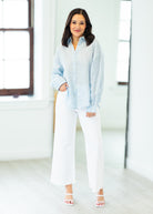 Woman wearing a light blue striped shirt and white pants in a bright room.