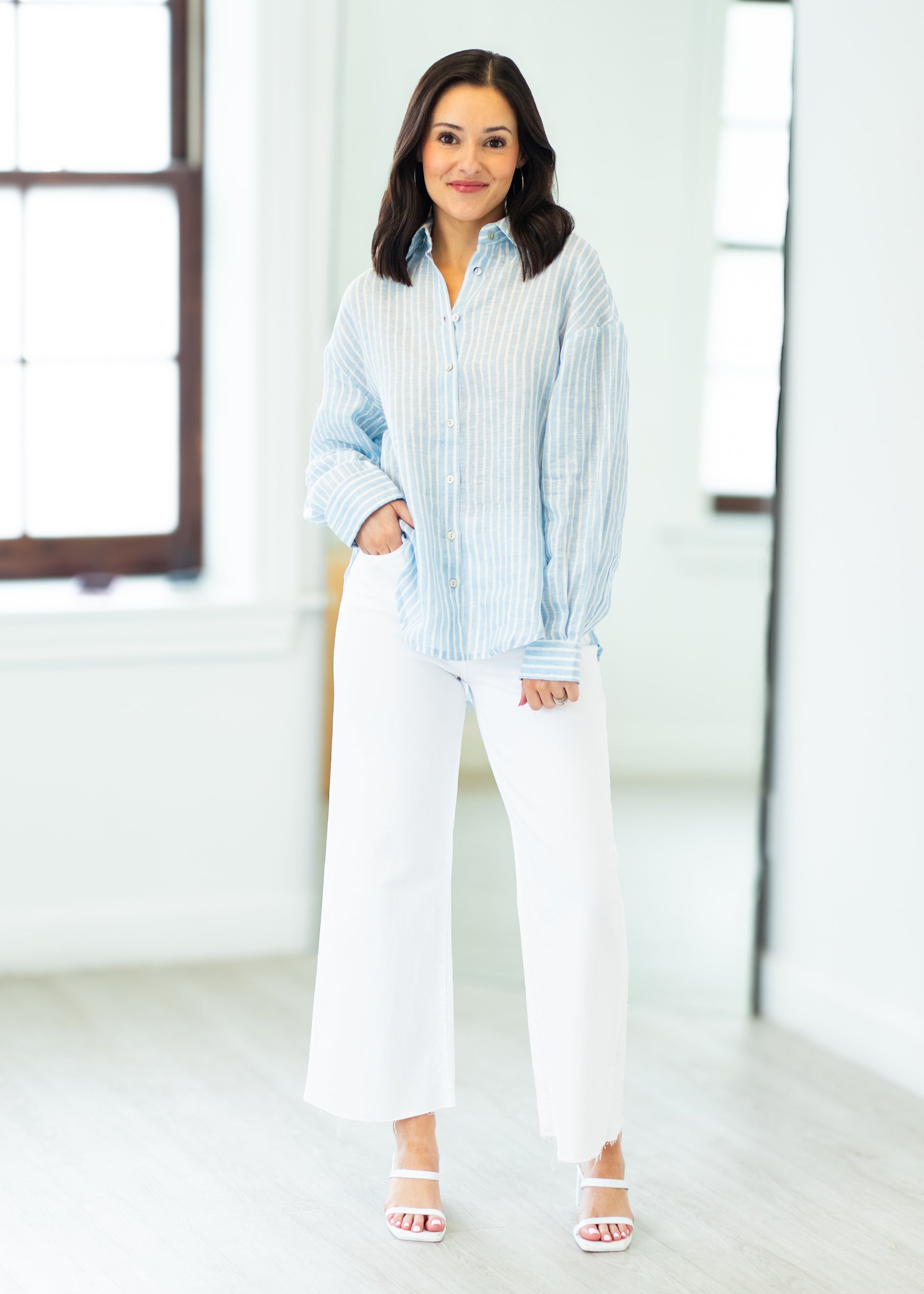 Woman wearing a light blue striped shirt and white pants in a bright room.