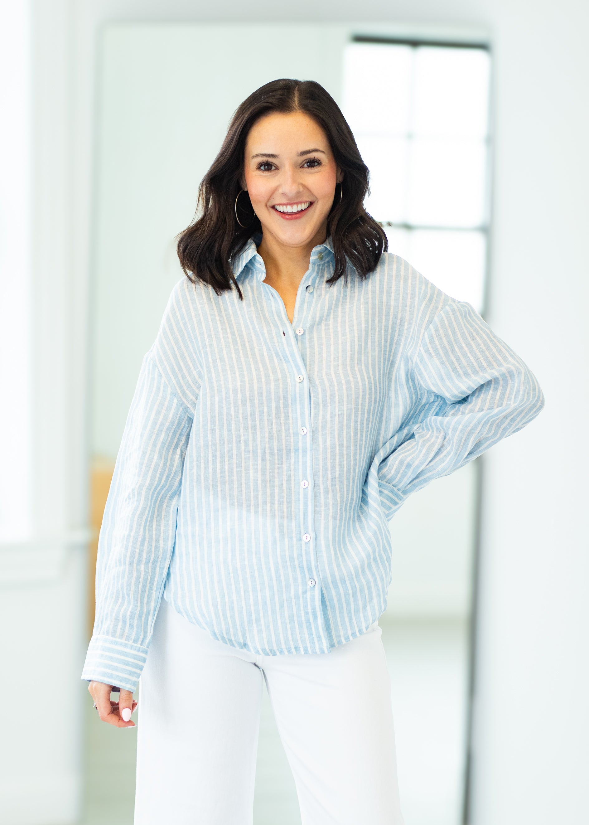 Woman wearing a light blue striped shirt and white pants in a bright room.