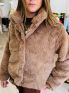 A woman wearing a brown faux fur jacket with a large collar, standing in a clothing store.