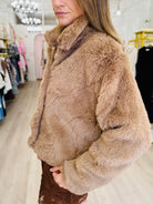 A woman wearing a plush, light brown faux fur jacket in a boutique setting.