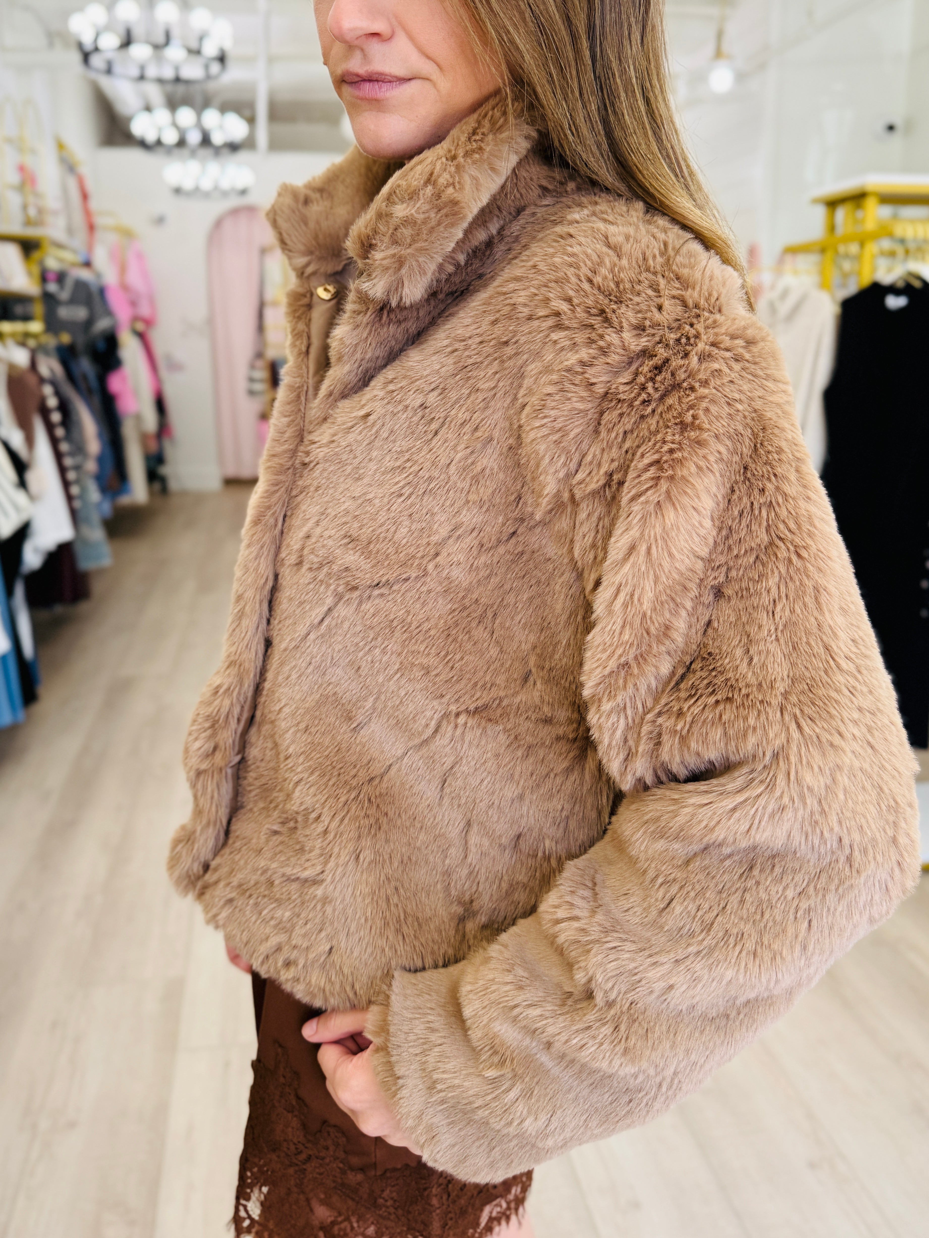 A woman wearing a plush, light brown faux fur jacket in a boutique setting.