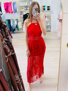 A woman takes a mirror selfie in a clothing boutique wearing a bright red crochet halter dress with a fringe hem.