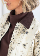 Close-up of a person wearing a cream corduroy jacket with black mottled speckles and a dark brown ribbed collar, layered over a dark brown turtleneck sweater.