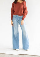 A model wearing a rust-colored, wide-sleeve knit top and light blue wide-leg denim jeans, standing against a plain white studio background.