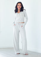 A woman modeling a light heather gray lounge set consisting of a long-sleeve half-zip top and matching wide-leg sweatpants, standing in a bright, minimalist room.