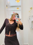 A woman takes a mirror selfie in a fitting room wearing a matching black and white polka dot two-piece set consisting of a long-sleeve tie-front crop top and a high-waisted skirt.