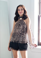 A woman modeling a sleeveless leopard-print halter top with sheer flutter sleeves and black lace-trimmed shorts in a bright indoor setting.