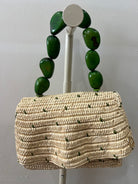 Woven handbag with green bead handles on a gray background