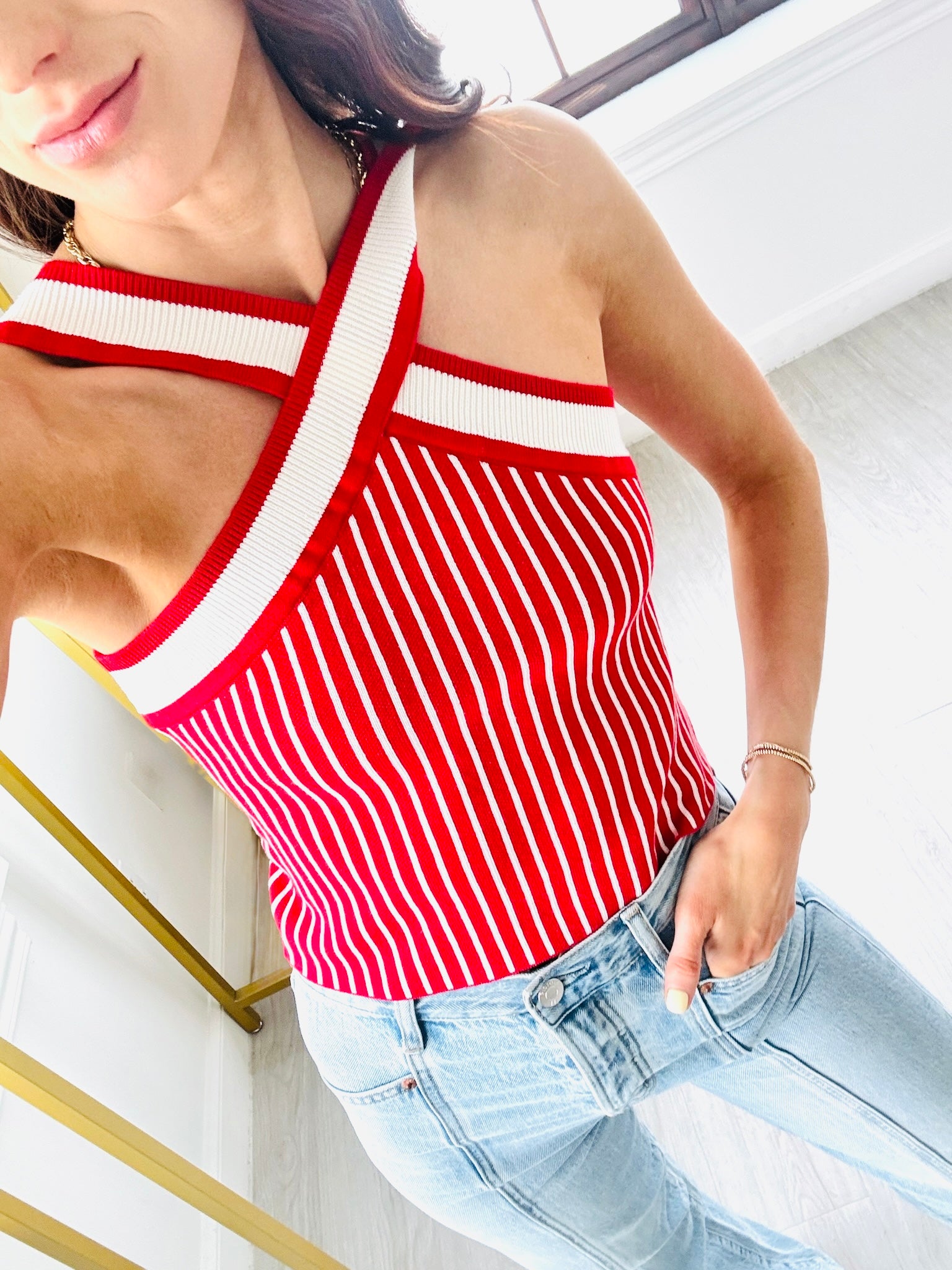 Woman wearing a red and white striped tank top and light blue jeans indoors.