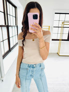 Woman taking a mirror selfie wearing a beige off-shoulder top and light blue jeans.