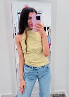 A woman taking a mirror selfie in a boutique, wearing a pale yellow sleeveless top and light blue jeans.