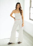 Woman wearing a white strapless jumpsuit with black polka dots in a minimal indoor setting.