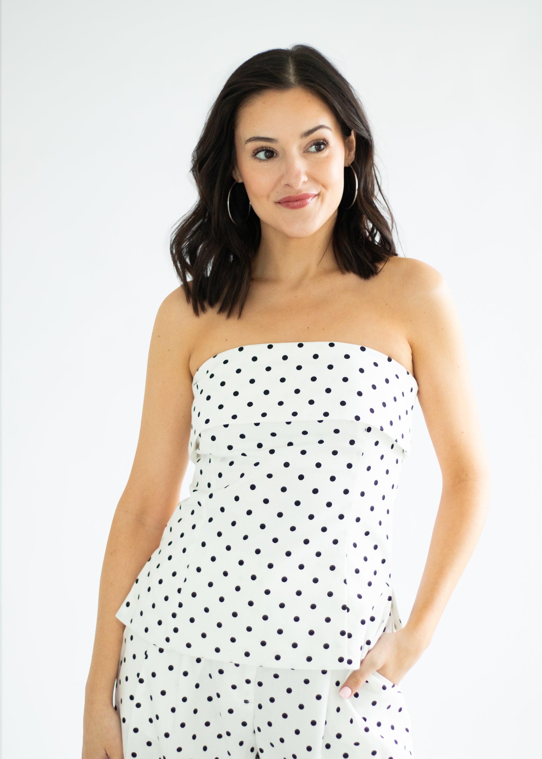 Woman wearing a white strapless dress with black polka dots on a white background