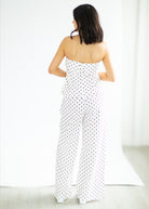 Woman wearing a white strapless jumpsuit with black polka dots on a white background