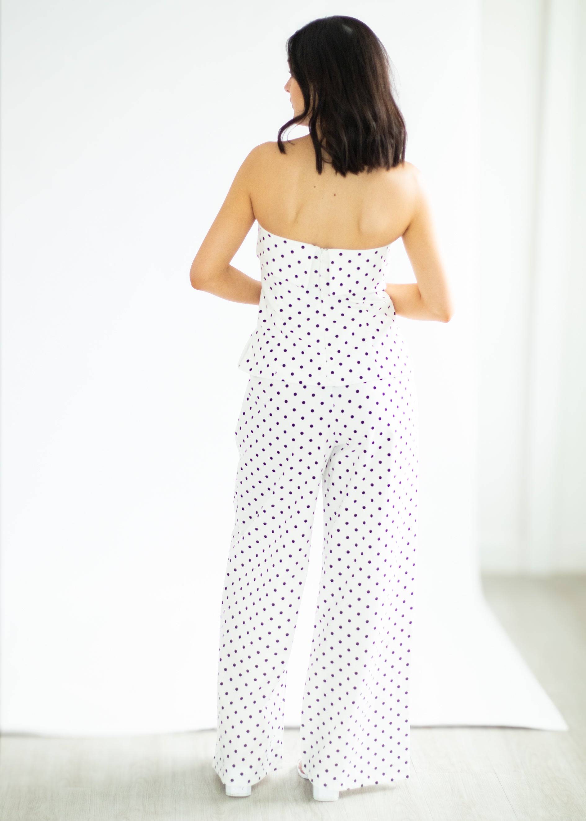 Woman wearing a white strapless jumpsuit with black polka dots on a white background