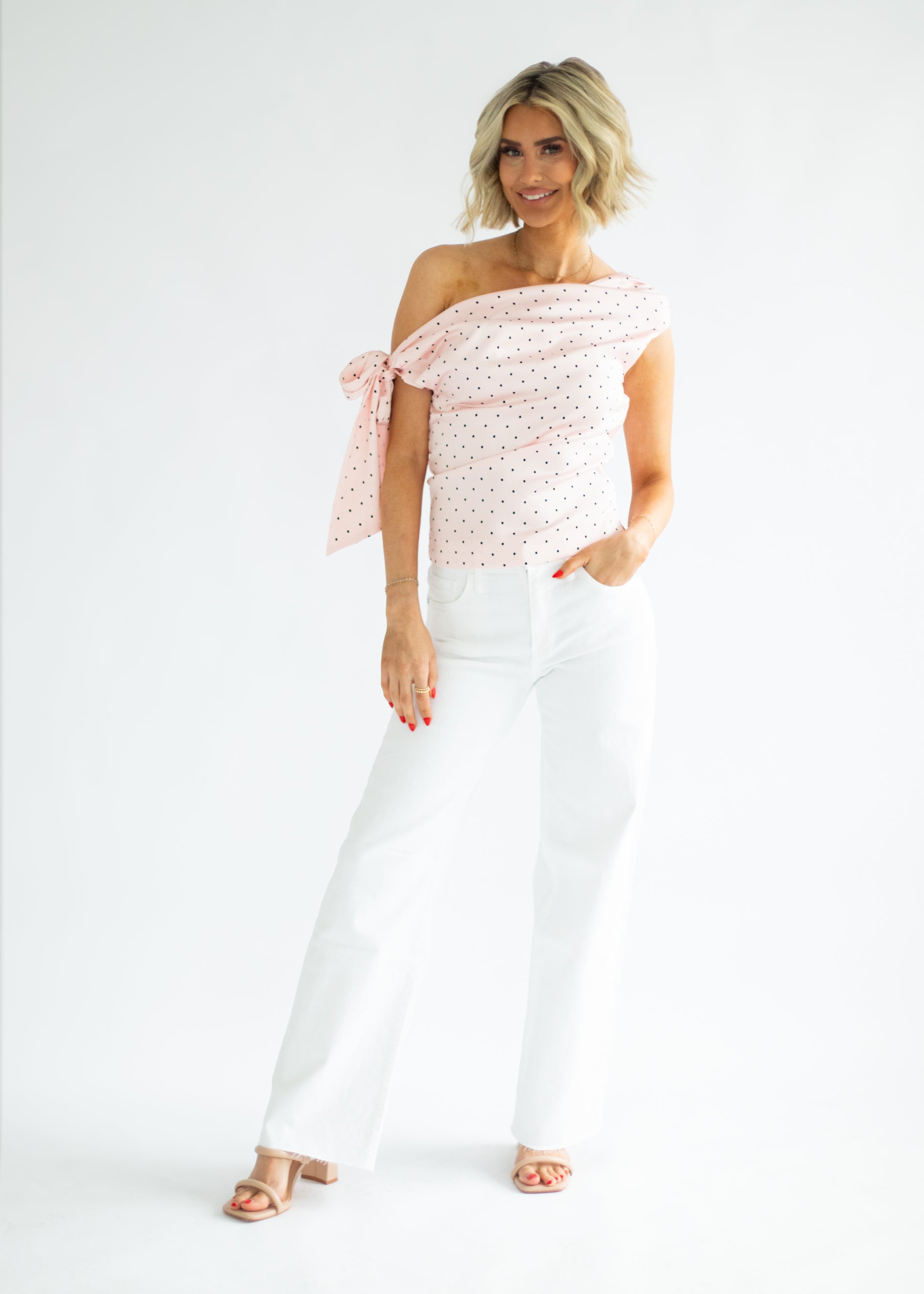 Woman wearing a white off-shoulder top with pink floral pattern and white pants on a white background