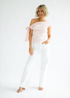 Woman wearing a white off-shoulder top with pink floral pattern and white pants on a white background