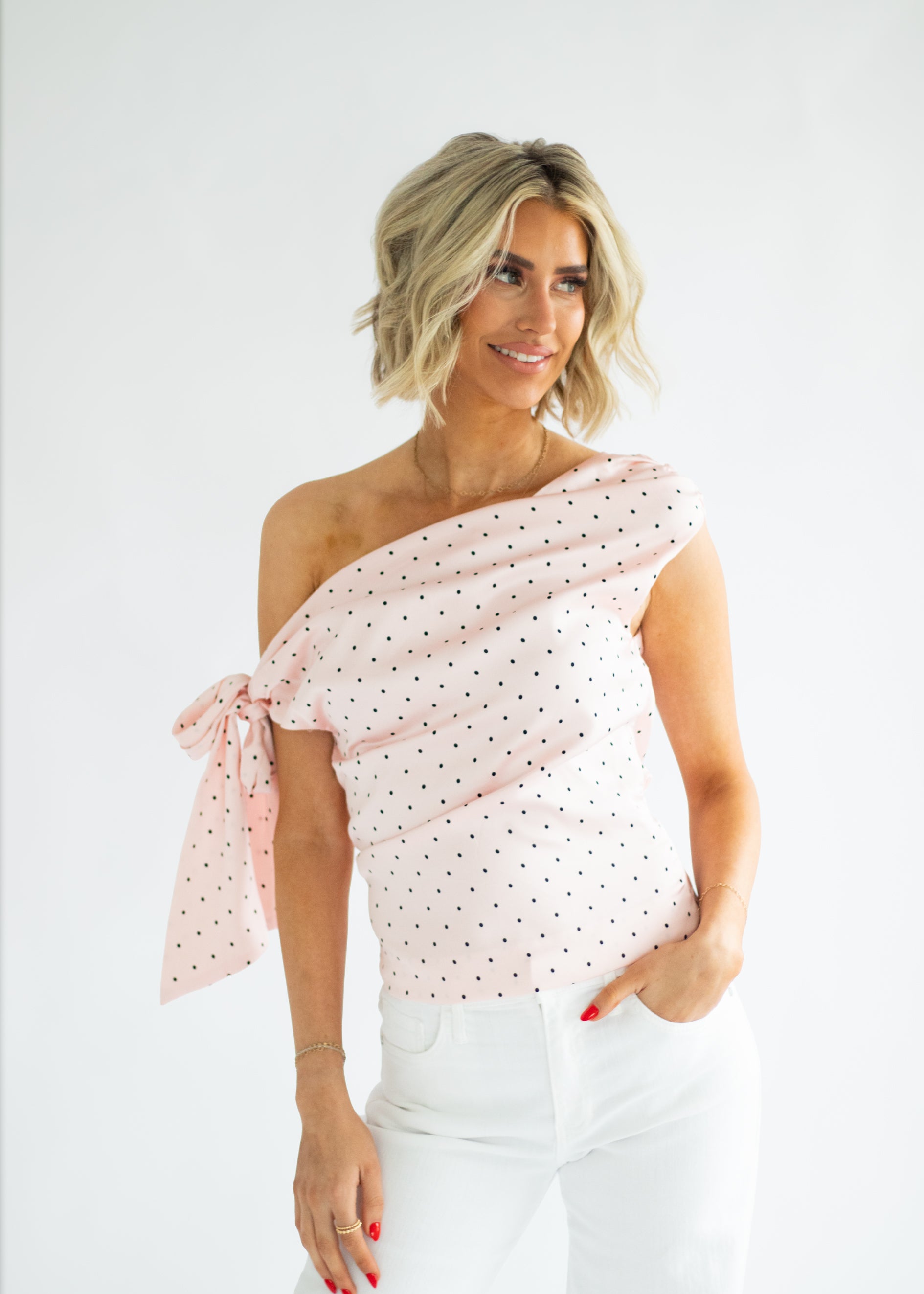 Woman wearing a one-shoulder polka dot top against a white background