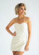 Woman wearing a strapless white dress against a plain background