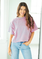 Woman wearing a pink and white striped shirt and light blue jeans indoors.
