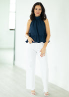 Woman wearing a navy top and white pants against a white background
