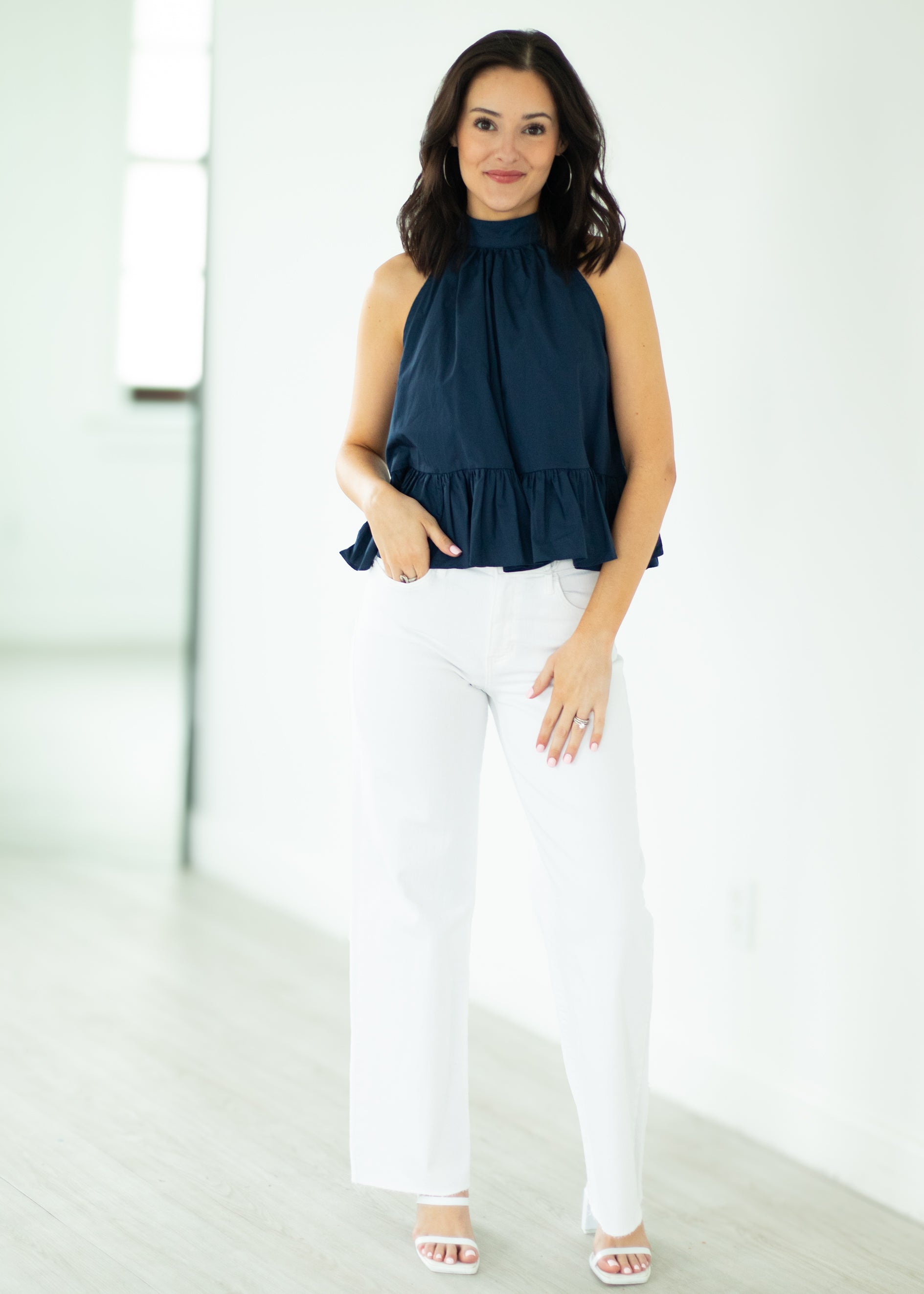 Woman wearing a navy top and white pants against a white background