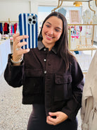 A woman taking a mirror selfie in a boutique, wearing a dark brown corduroy button-up shirt jacket with a pointed collar and front flap pockets.