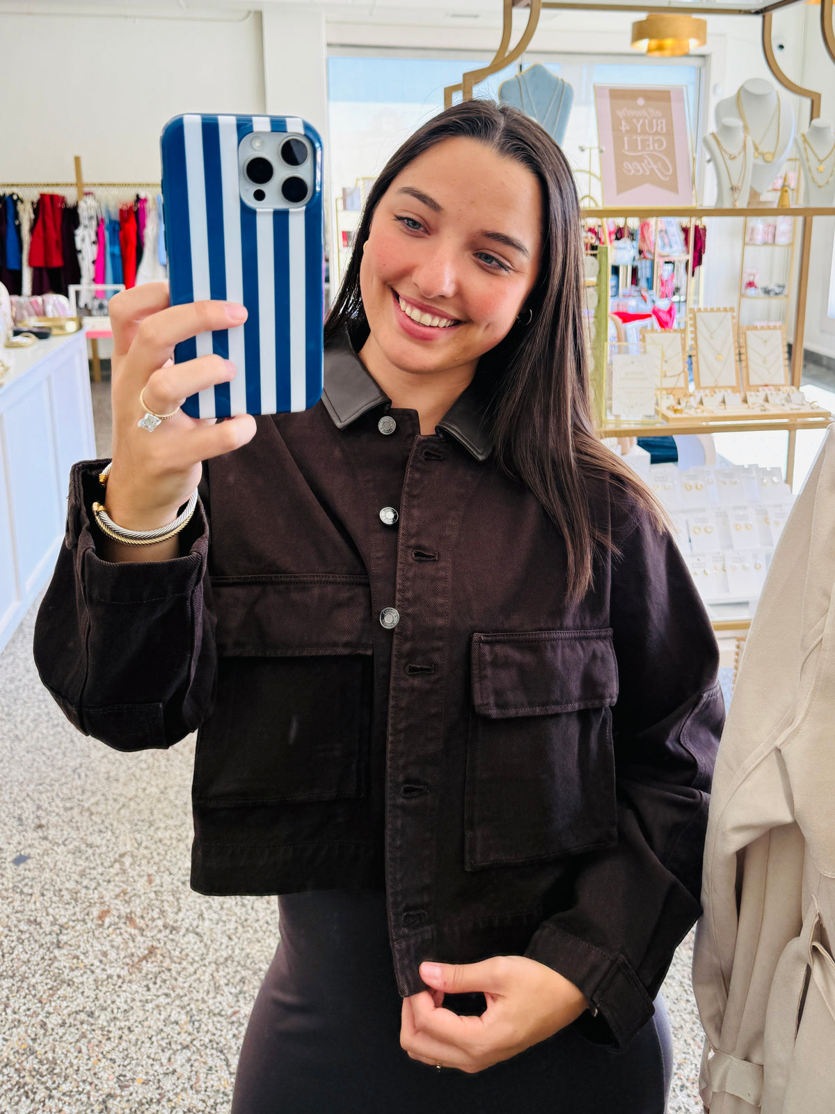A woman taking a mirror selfie in a boutique, wearing a dark brown corduroy button-up shirt jacket with a pointed collar and front flap pockets.