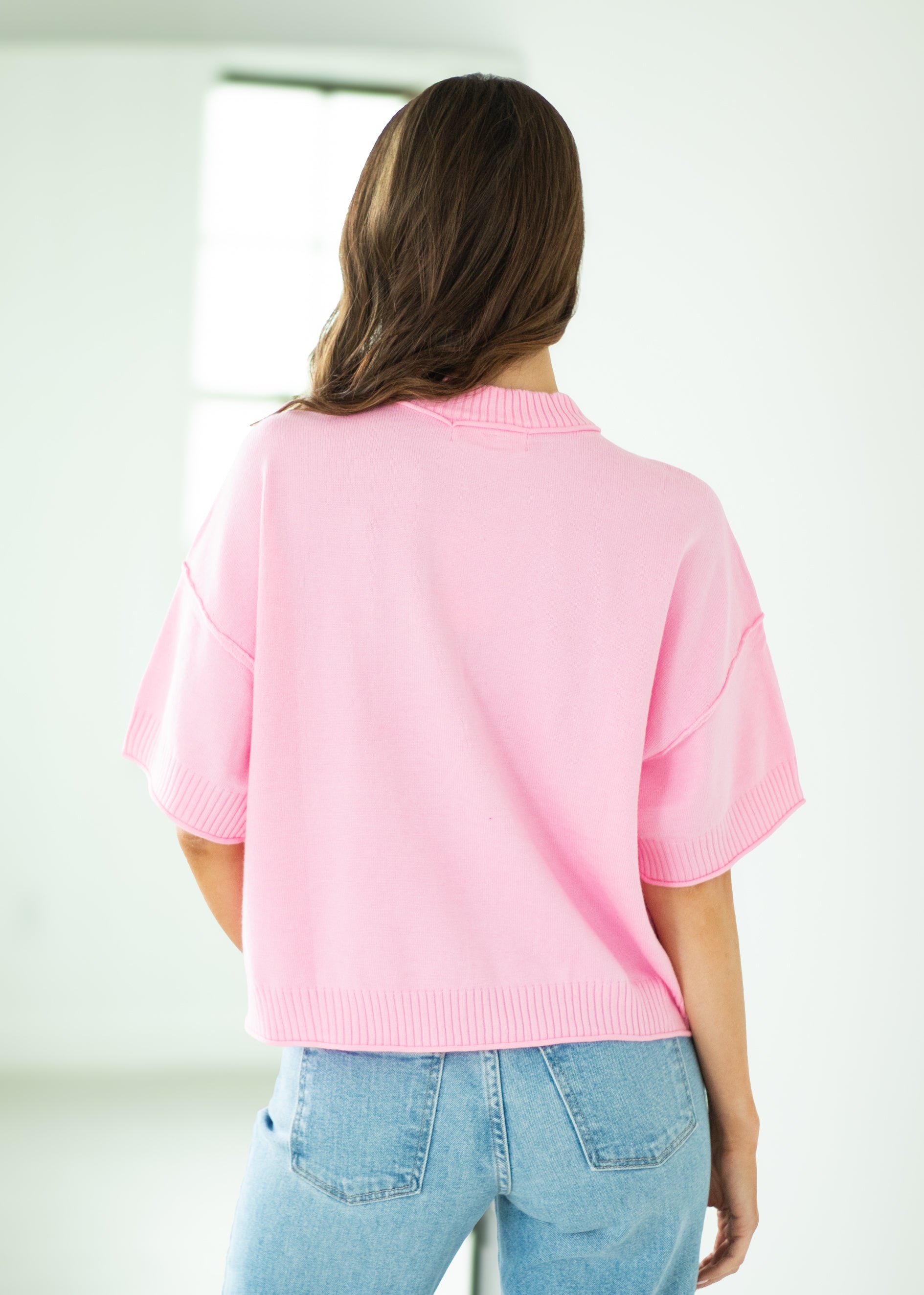 Person wearing a pink sweater and blue jeans in a minimal indoor setting