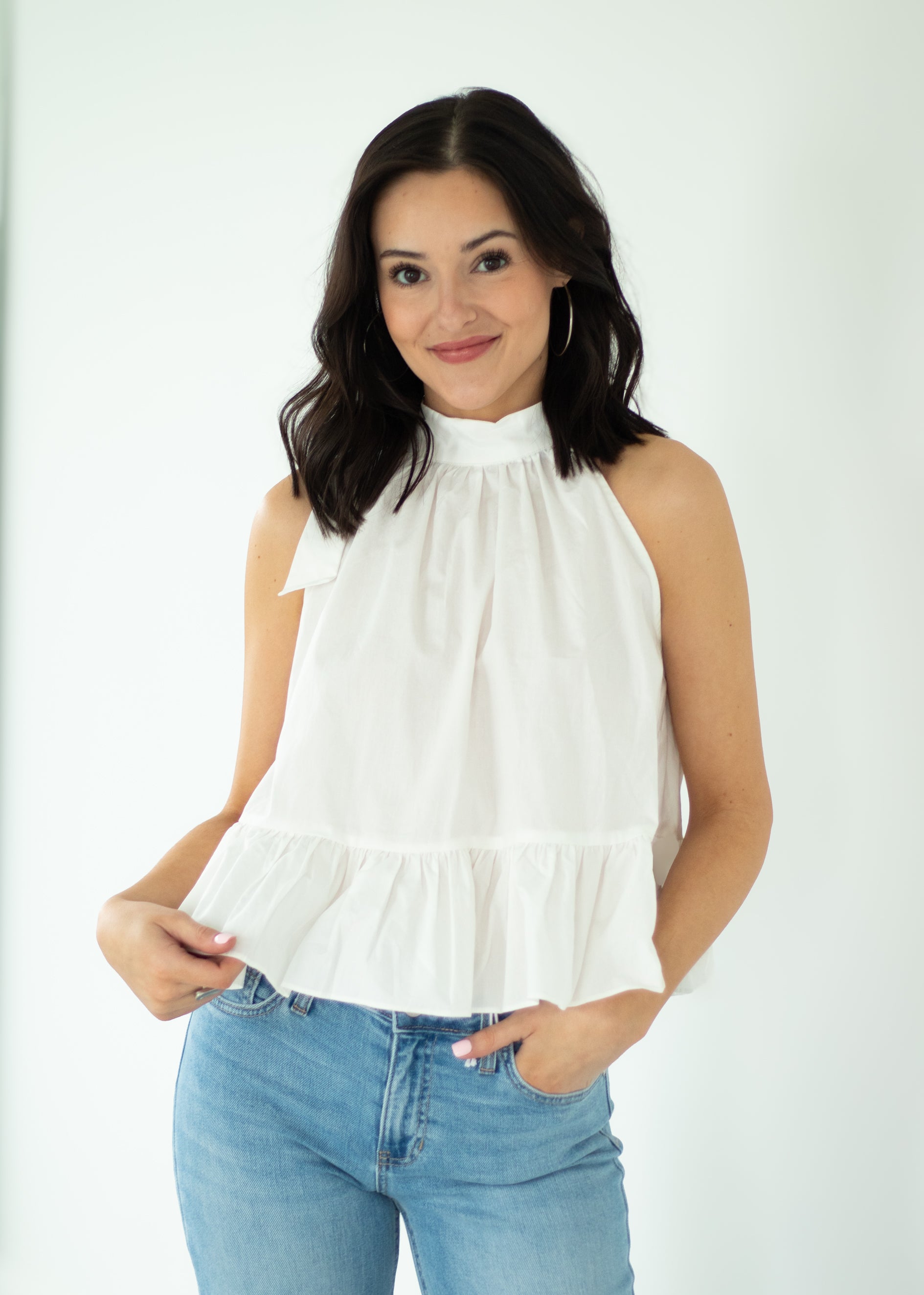 Woman wearing a white sleeveless top and blue jeans against a white background