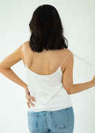 Person wearing a white spaghetti strap top and blue jeans on a plain background