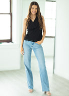 Woman wearing a black sleeveless top and light blue jeans in a bright room.