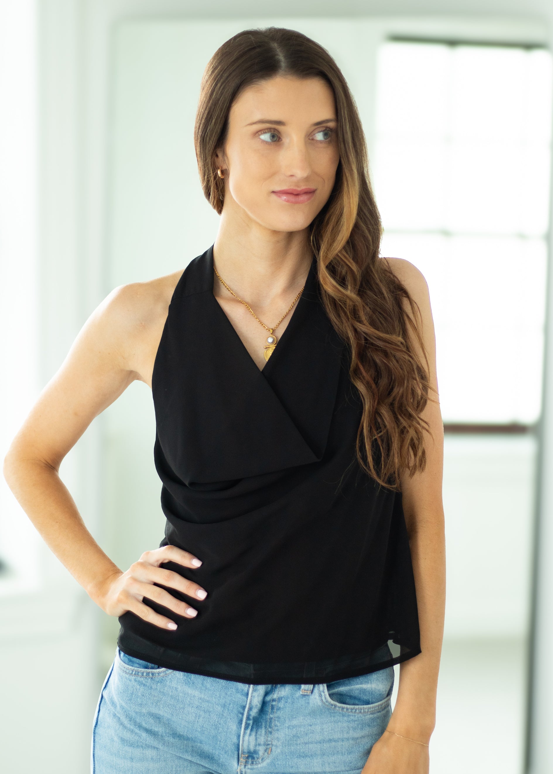 Woman wearing a black sleeveless top and blue jeans indoors.