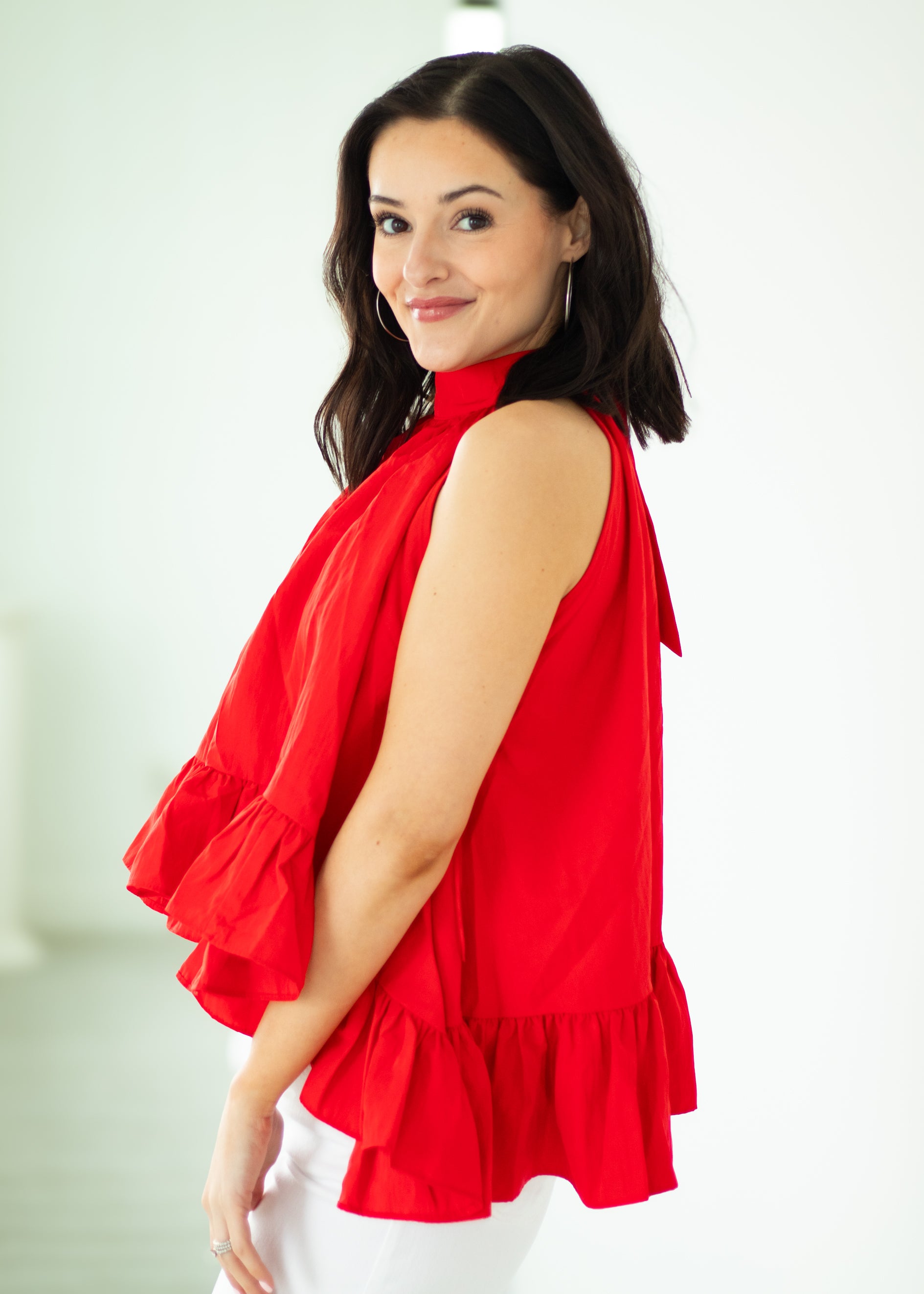 Woman wearing a red sleeveless blouse with ruffled details on a white background