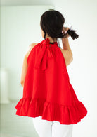 Person wearing a red halter top with ruffled layers on a white background